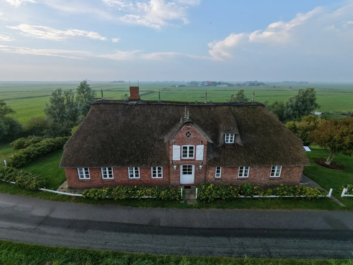 Drohnenaufnahme von Haus Westerschütting zwischen grünen Wiesen unter dem weiten Pellwormer Himmel