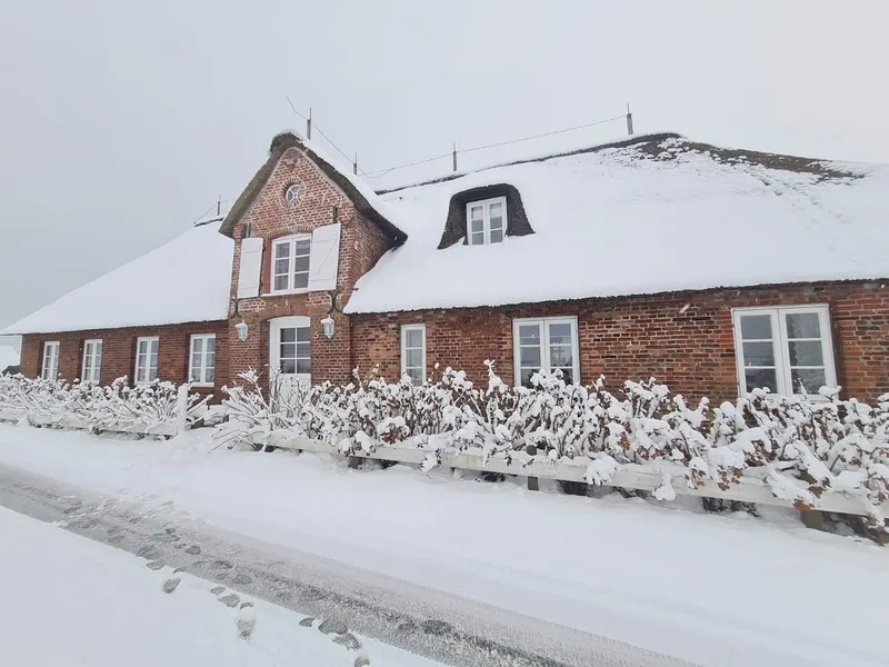 Haus Westerschütting unter einem verschneiten Reetdach im Winter